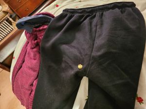 Picture of a pair of black tracksuit bottoms laid on a bed with a red top beside them. Stuck to the bum is a piece of popcorn