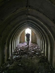 distant Silhouetted figure leaving through a bright open door with light falling on a vaulted ceiling and leaf litter strewn floor 