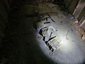 Torchlit concrete floor with some rubble and evidence of a wall and a narrow doorway