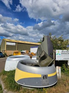 Plane parts lying against a shed with a light industrial unit in the background and a cloudy and blue sky